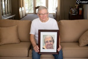 Man sitting on a couch holding a photo of his deceased wife.