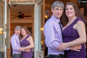 Woman in tight and flattering purple dress hugging man dressed in purple tie and shirt in front of Pompette cocktail bar.